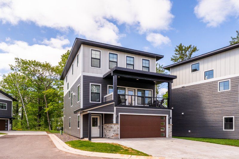 Modern three‑story gray townhouse with a two‑car garage and second‑floor balcony in a suburban setting